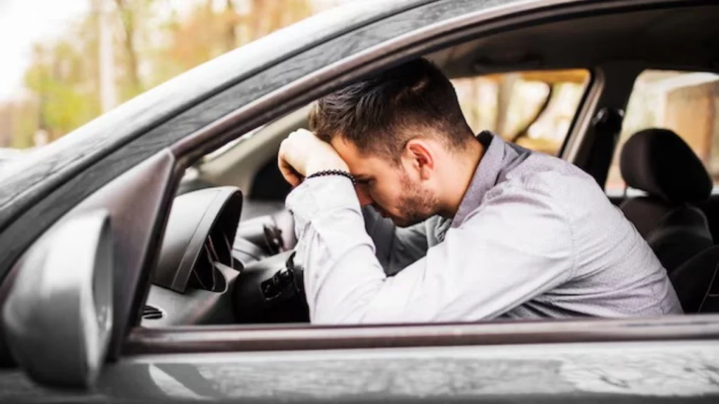 Foto de uma pessoa dentro de um automóvel e expressando tristeza com seu carro