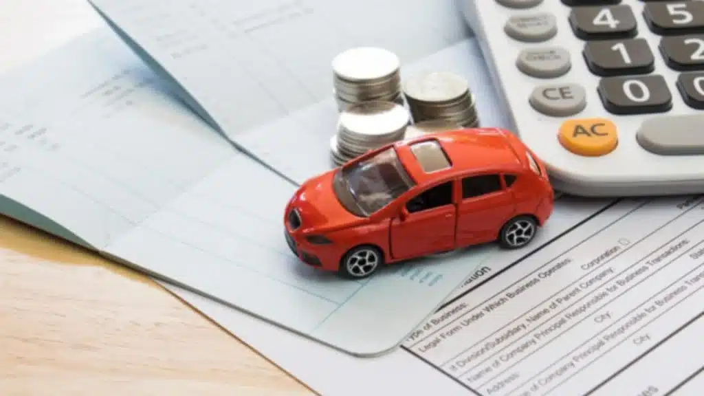 Imagem de um carro de brinquedo sob a mesa, com algumas moedas e documentos ao lado, fazendo alusão a pauta sobre financiamento de veículos e seu recorde no Brasil em 2026