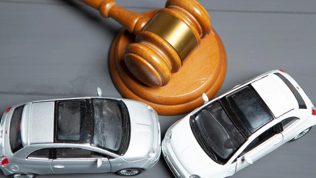 Imagem ilustrativa de dois carros na cor branca e um martelo de tribunal na cor madeira