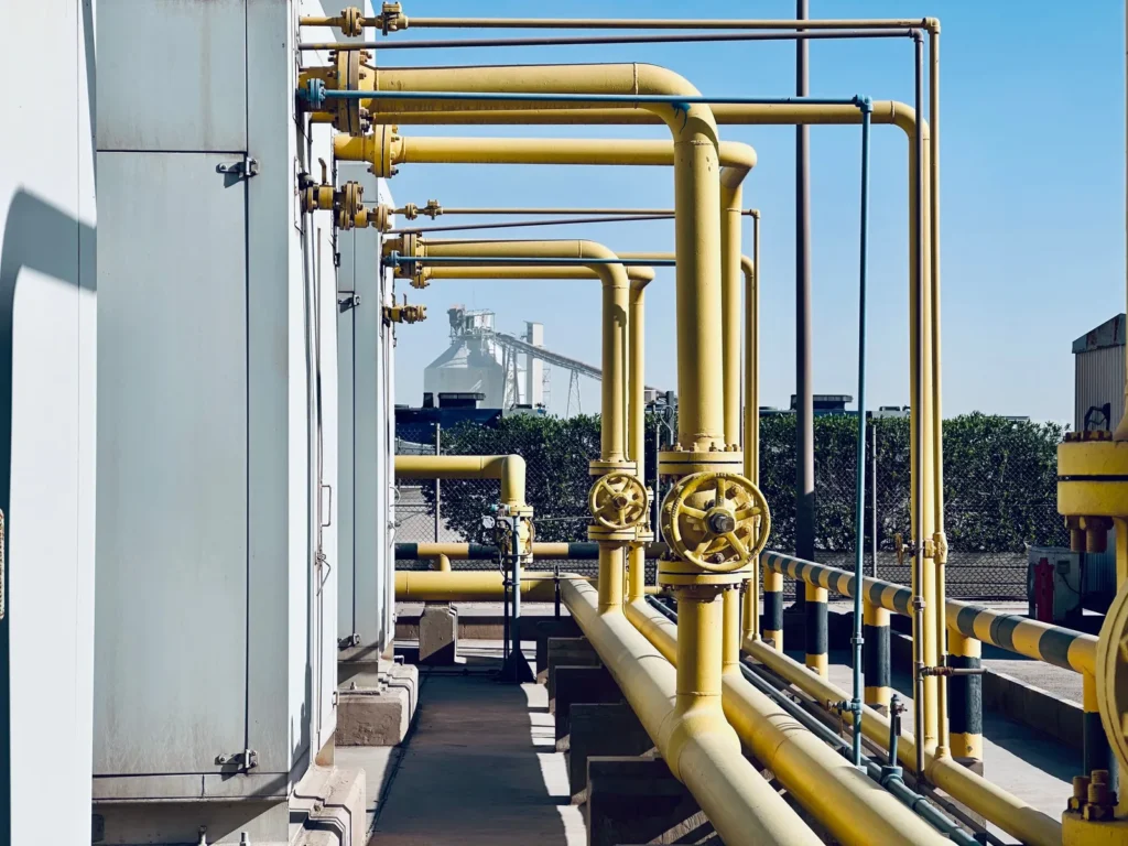 Tubulações industriais amarelas com válvulas em área externa.
