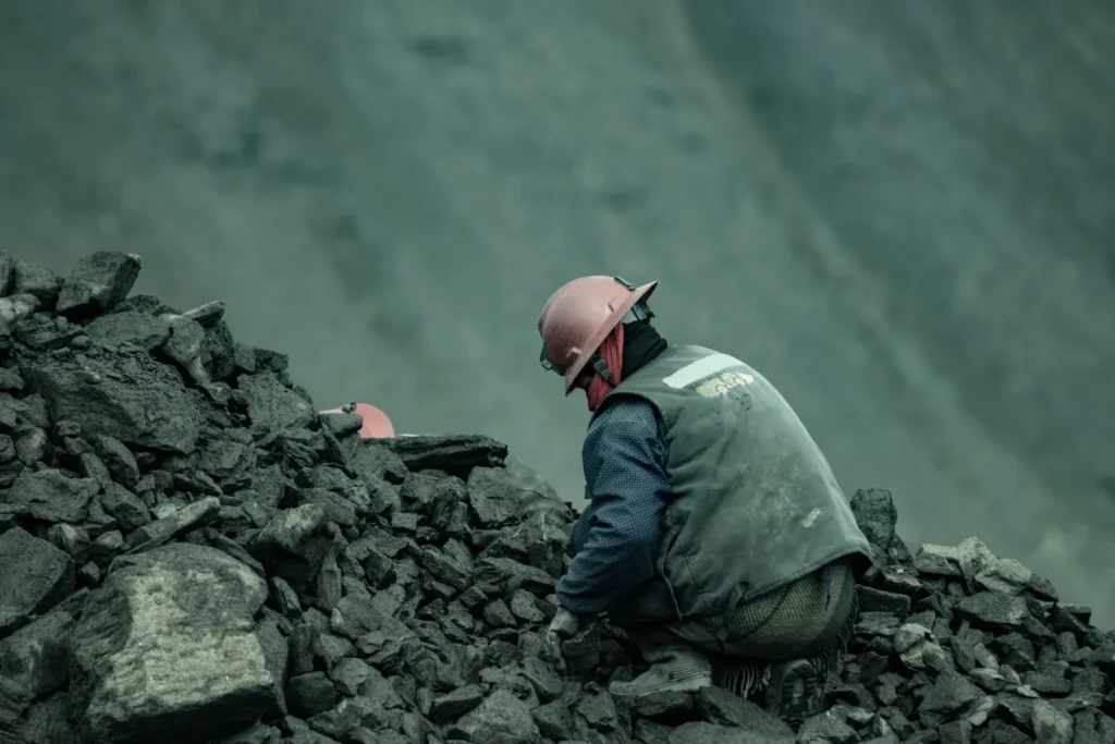Trabalhador com capacete de segurança inspecionando rochas em uma área de mineração.