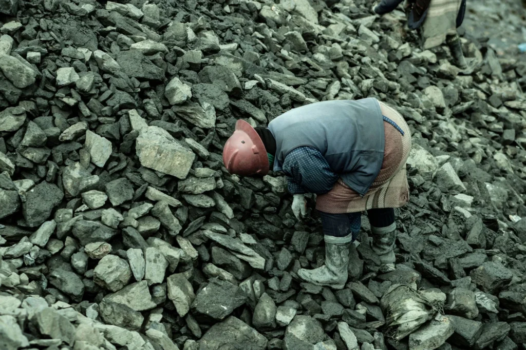 Trabalhador com capacete de segurança inspecionando monte de minério rochoso.