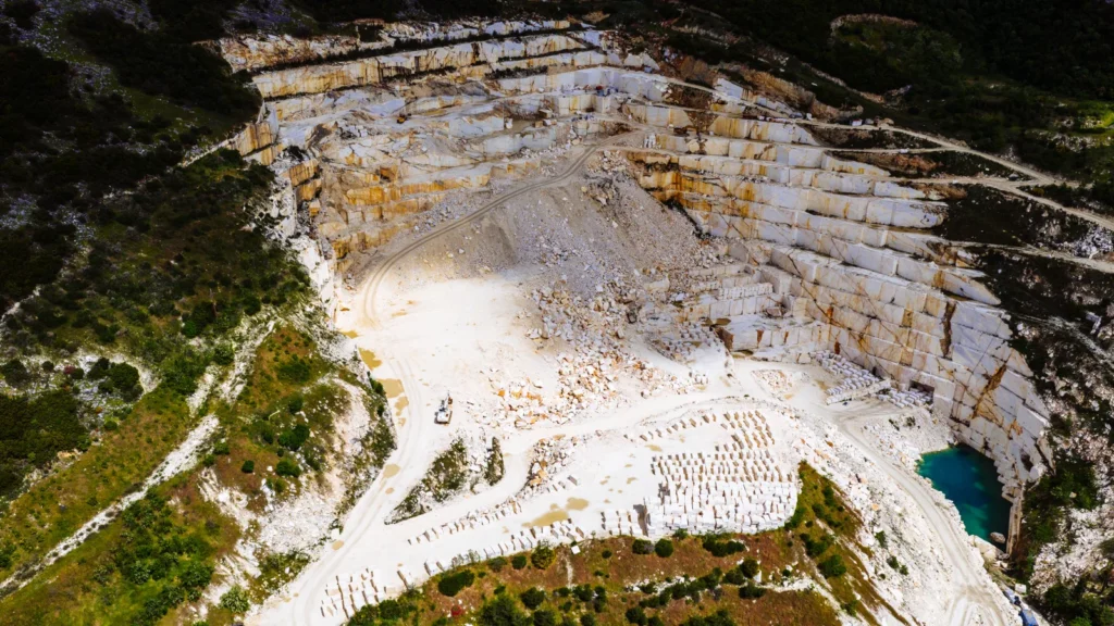 Vista aérea de grande pedreira de calcário com cavas profundas e lago de água azulada.
