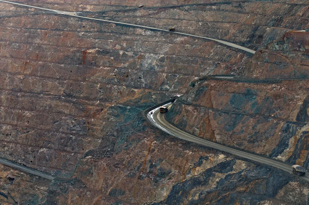 Vista aérea de mina a céu aberto com estradas sinuosas e caminhões de grande porte operando nos patamares.