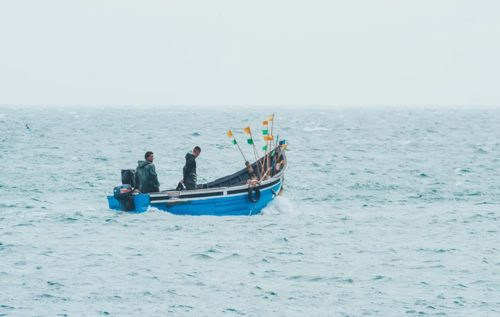 Pequeno barco azul com pescadores e bandeiras pequenas navegando no mar.