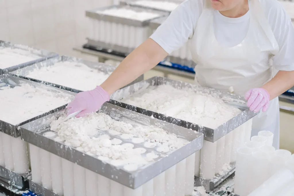 Operário em indústria de laticínios preparando derivados do leite em esteira de fábrica.