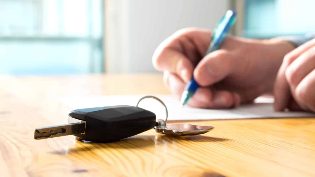 Imagem ilustrativa de uma pessoa assinando documento e com uma chave de carro em primeiro plano, tudo isso em alusão à pauta Adeus à papelada? Transferência de veículos pelo celular ganha força em 2026