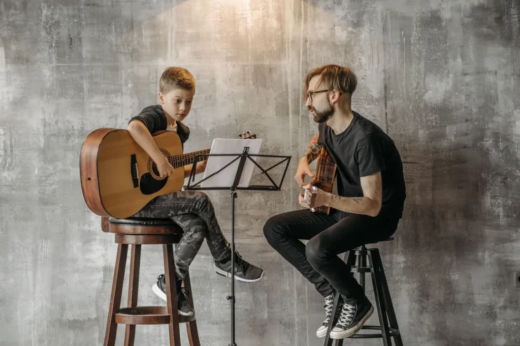 Professor de musica dando aula particular de violao para um aluno em um estudio iluminado