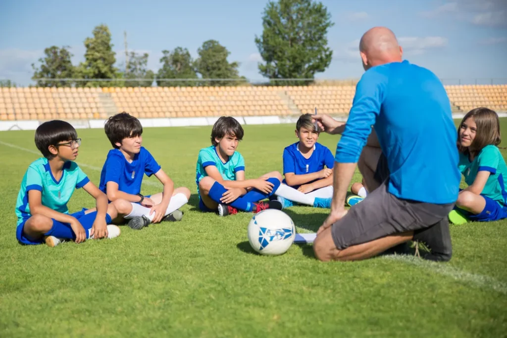 Professor de educação física ensinando crianças a jogar futebol em uma quadra